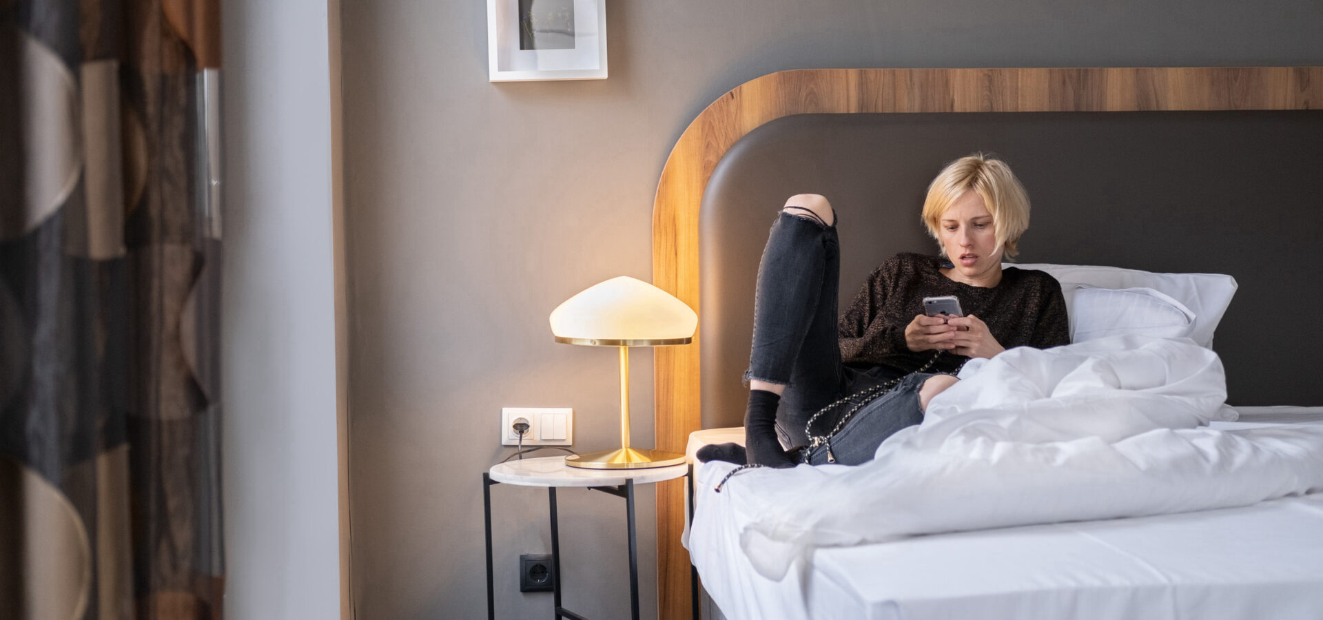 Frau sitzt mit ihrem Handy in der Hand auf dem Hotelbett